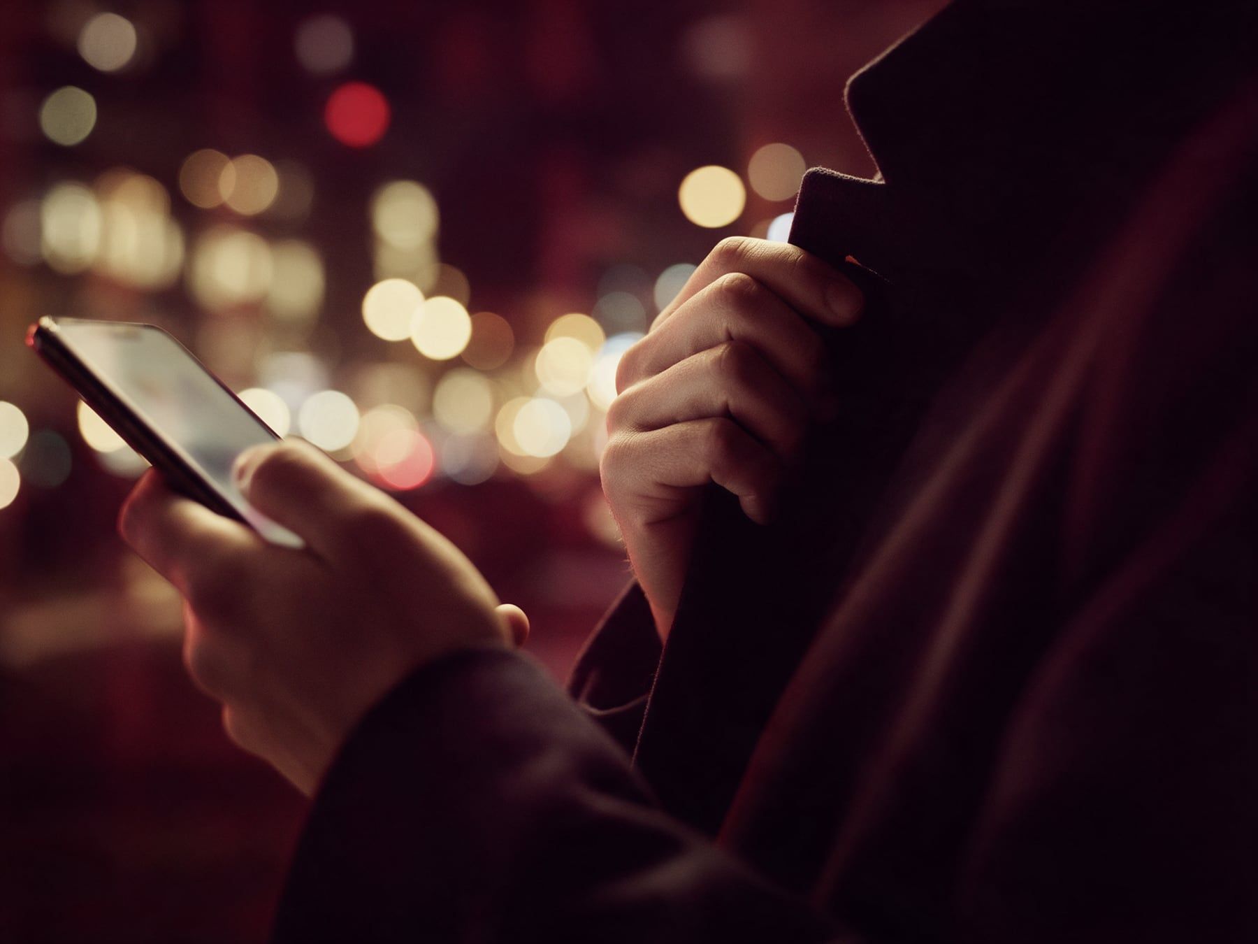 Une main tient un téléphone à l’écran flou, l’autre remonte le col d’un manteau