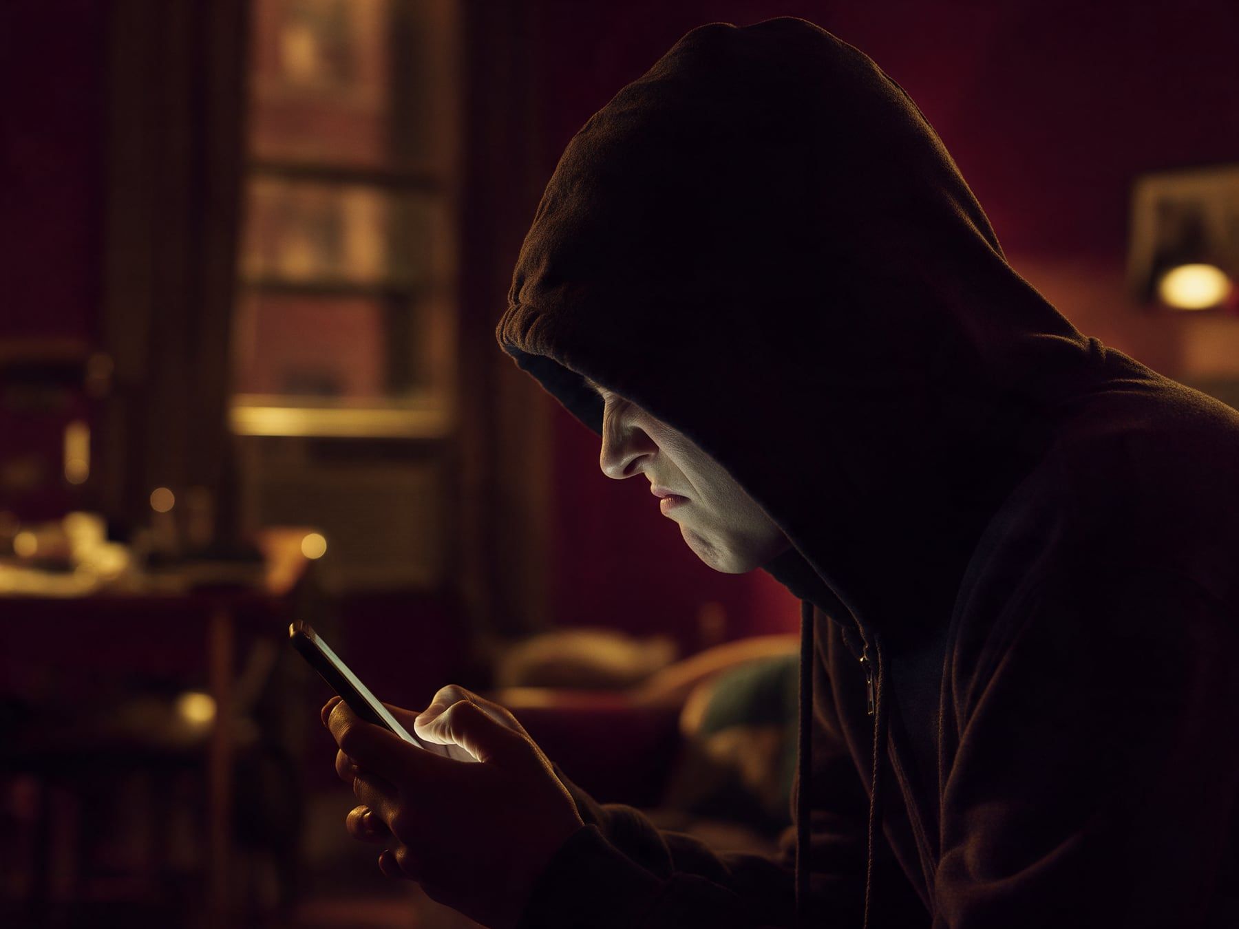 Une personne en capuche fronce les sourcils devant son téléphone